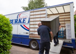 Burke Bros removal van with workers carrying a chest of drawers inside the van